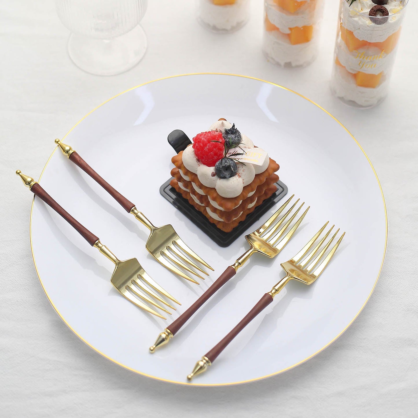 Gold and brown plastic dessert forks on a white plate with a dessert.