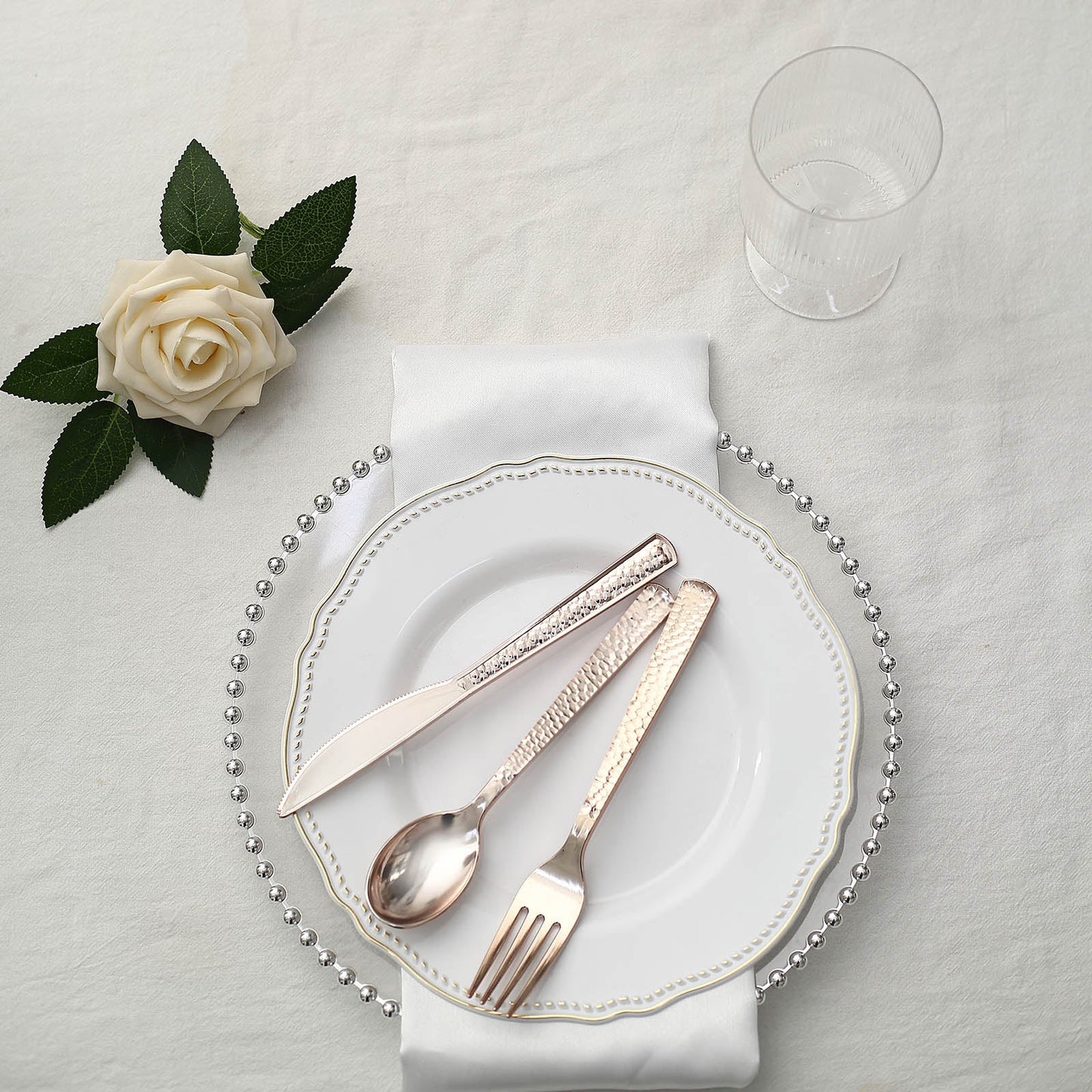 Hammered design rose gold heavy duty plastic silverware set on a white plate.