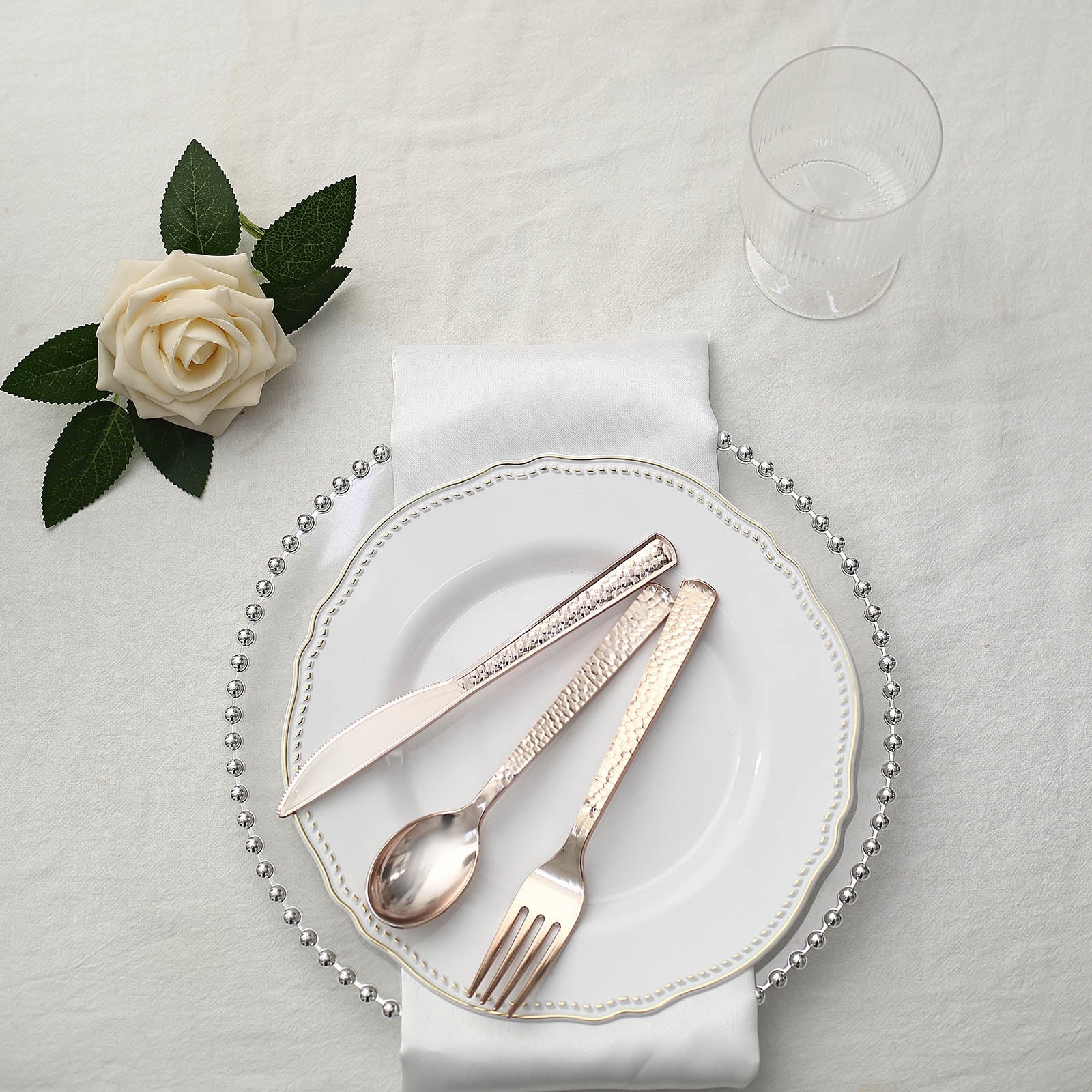 Hammered design rose gold heavy duty plastic silverware set on a white plate.
