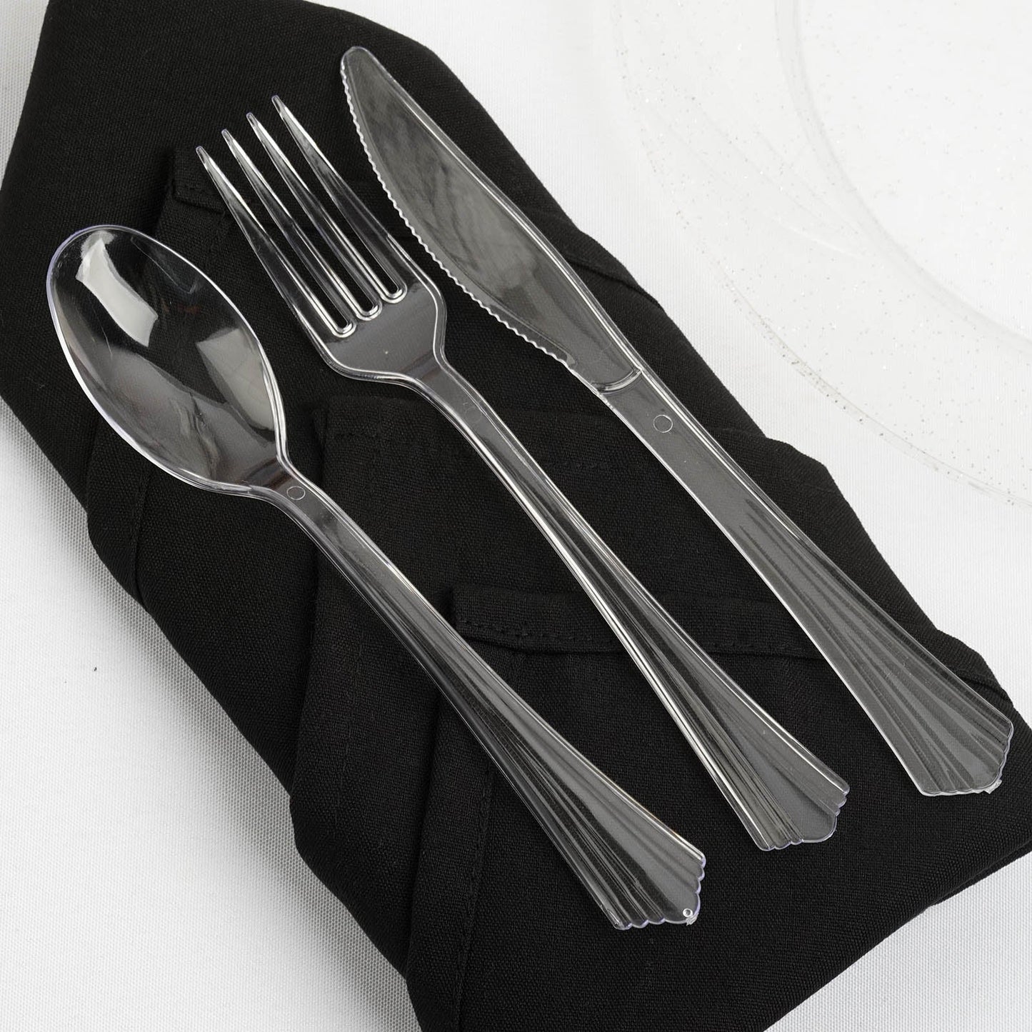 Clear plastic cutlery set on a black napkin for elegant dining.