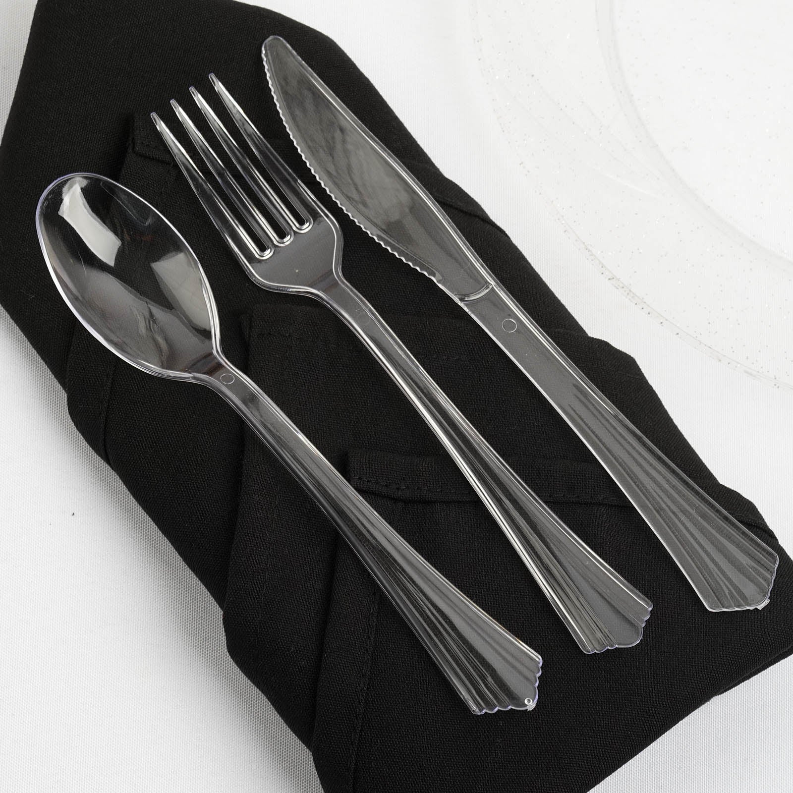 Clear plastic cutlery set on a black napkin for elegant dining.