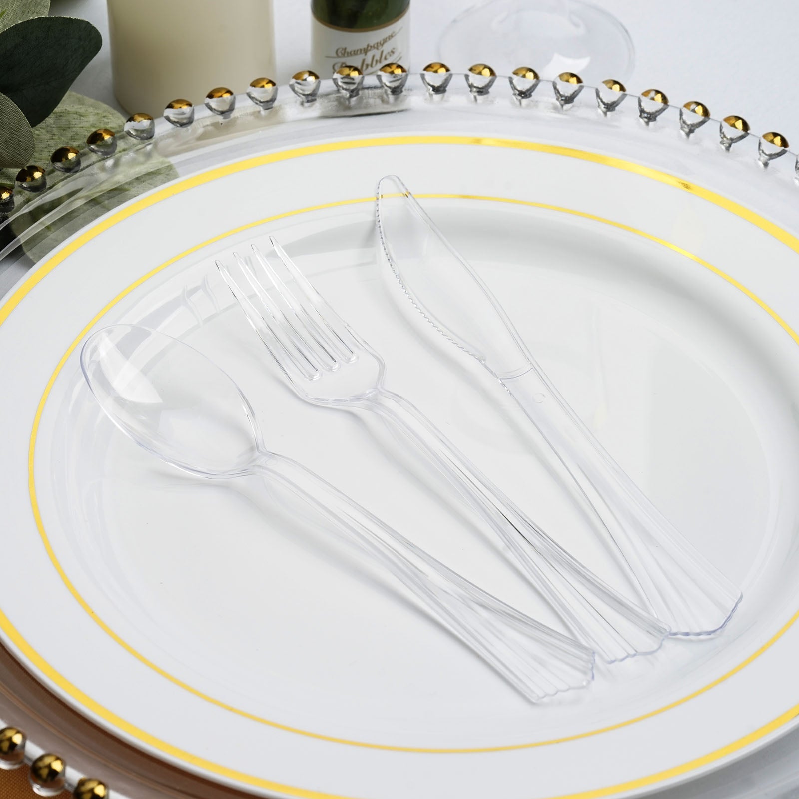 Elegant clear plastic cutlery on a decorative white plate with gold trim.