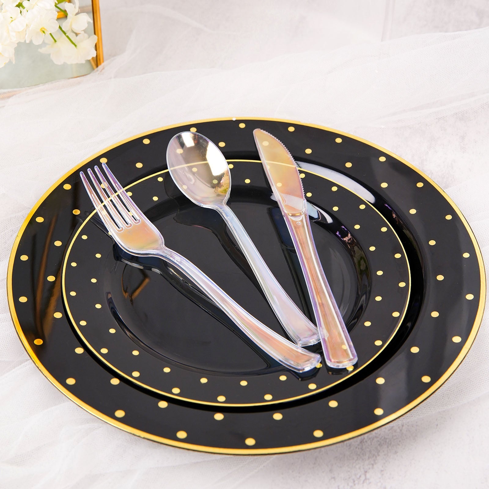 Iridescent disposable cutlery set on black plates with gold polka dots.
