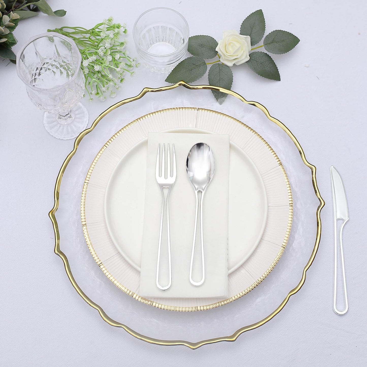 Silver 24 pack of modern disposable utensils on an elegant table setting.