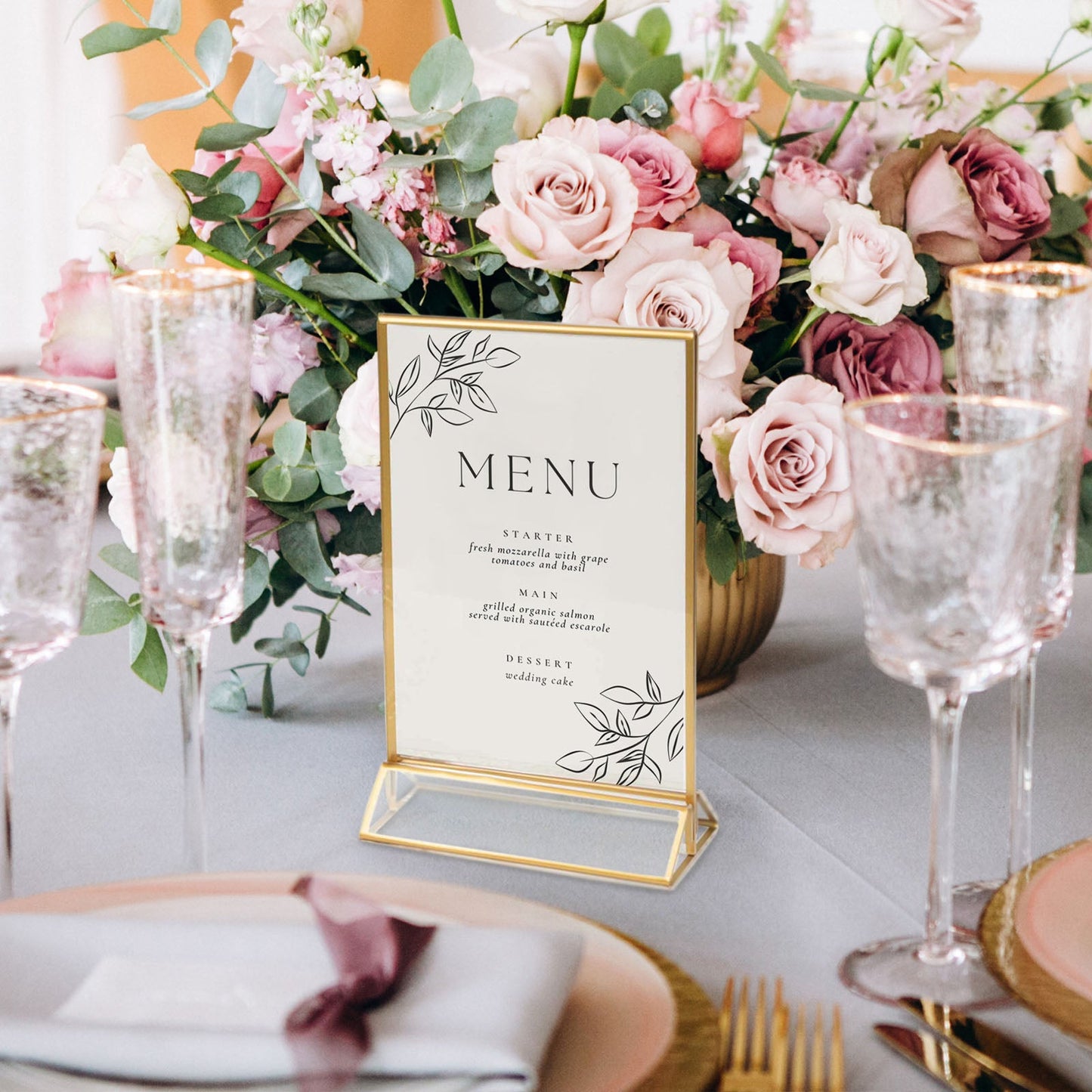 Gold freestanding table sign holder displaying a menu among pink flowers.