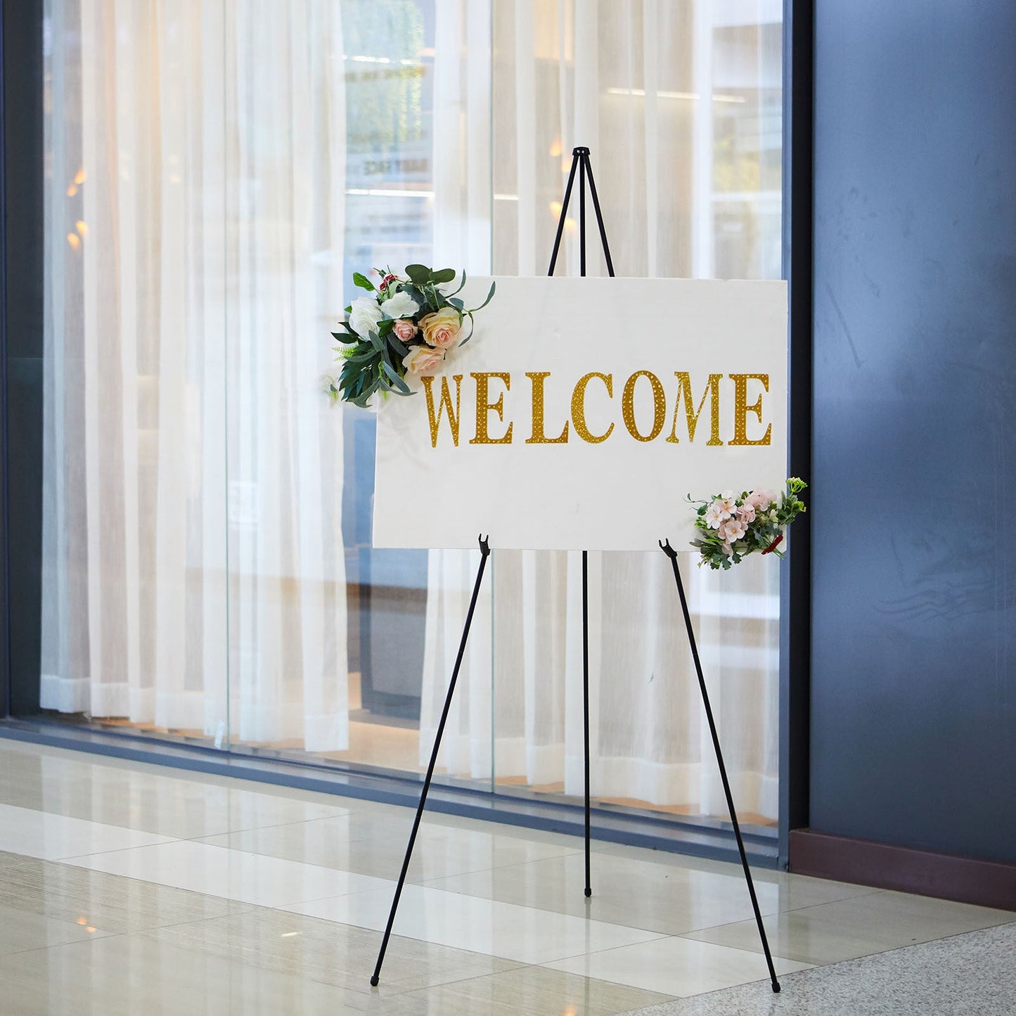 65" black metal easel stand displaying a welcome sign with floral accents.