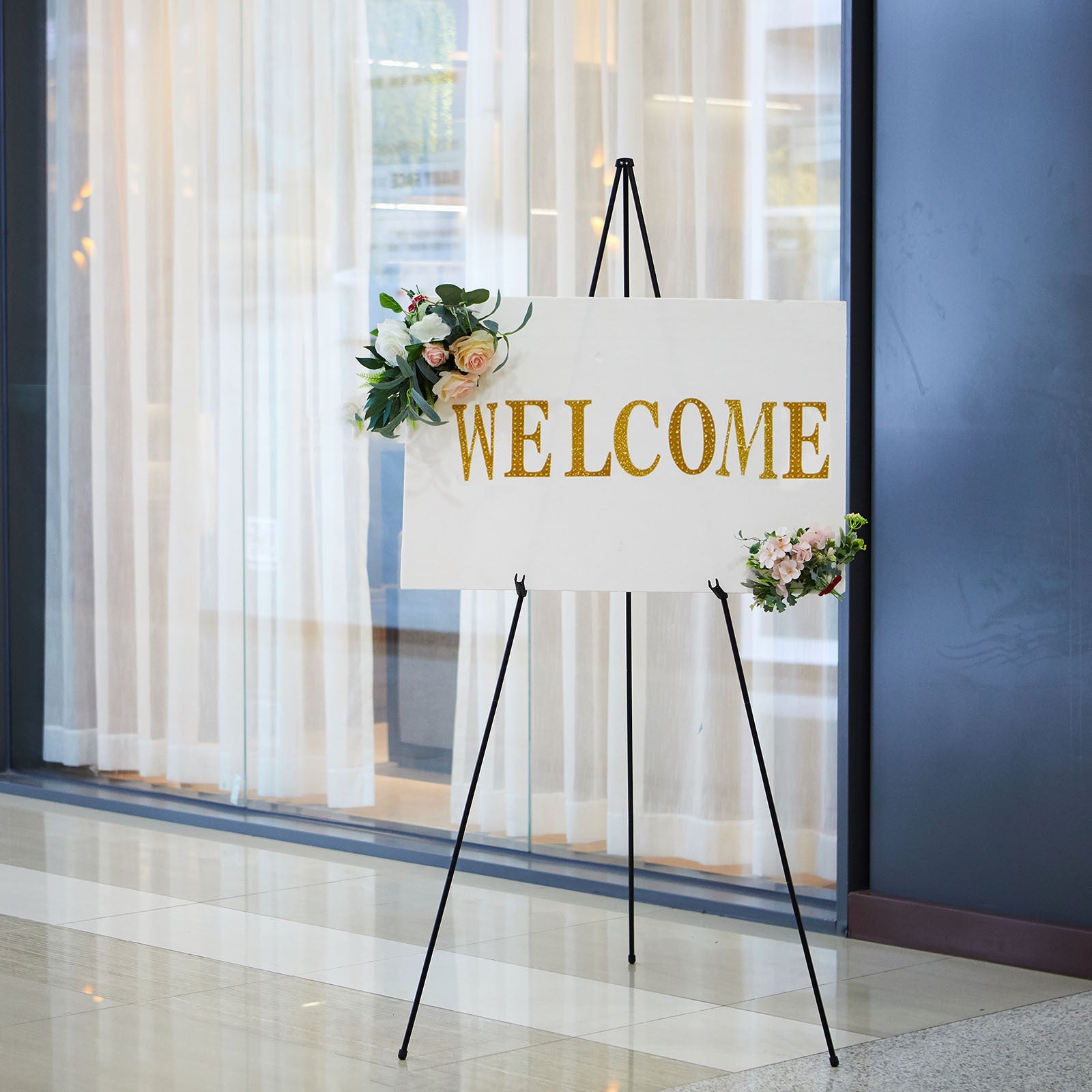 65" black metal easel stand displaying a welcome sign with floral accents.