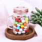 Rustic clear glass mason jar with rose gold lid filled with colorful candies.