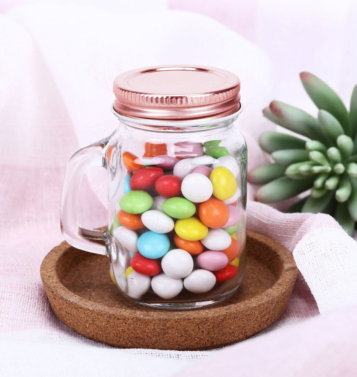 Rustic clear glass mason jar with rose gold lid filled with colorful candies.