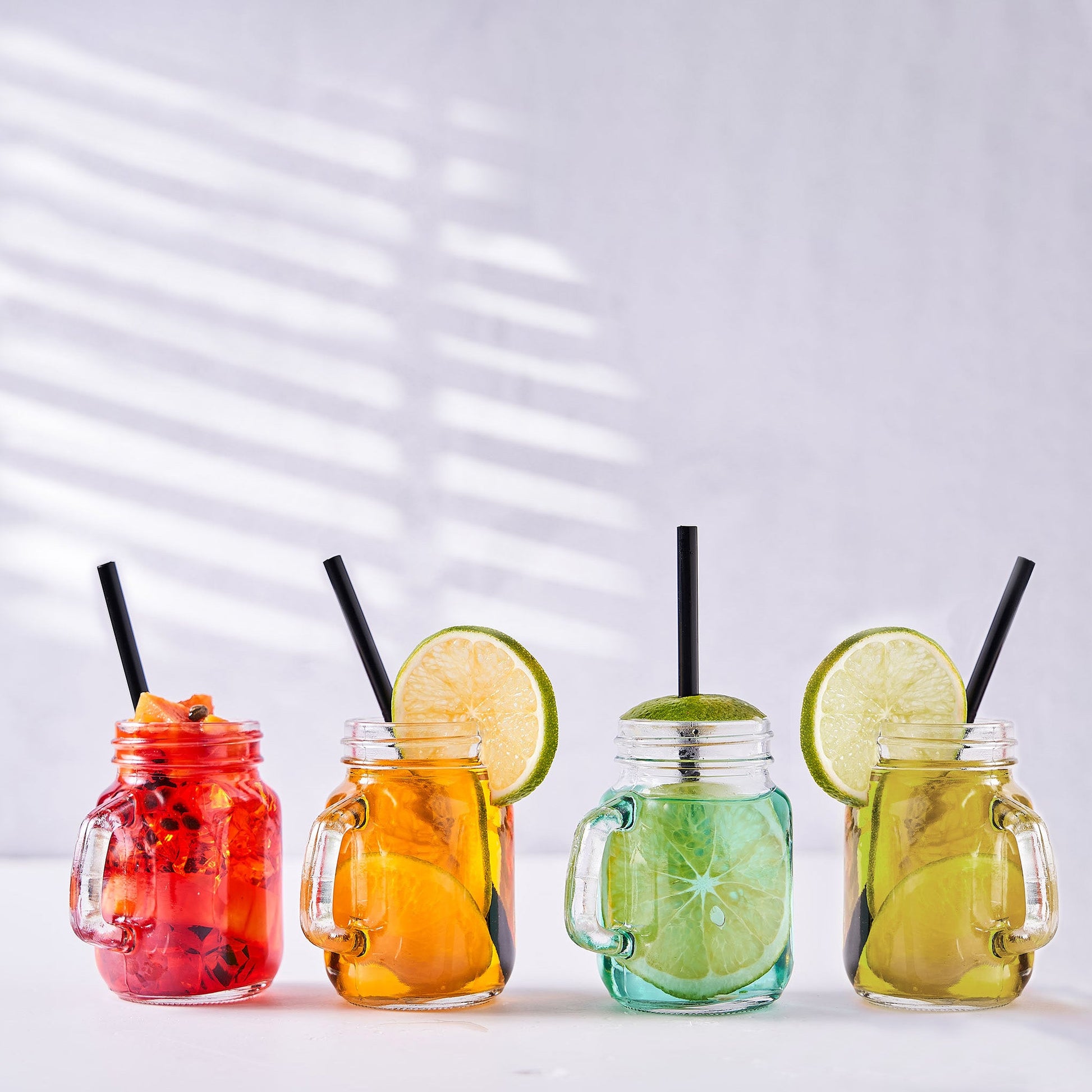 Rustic clear glass mason jars with handles and rose gold lids filled with colorful drinks.