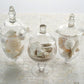 Clear glass apothecary jars with snap-on lids and decorative footed bases.
