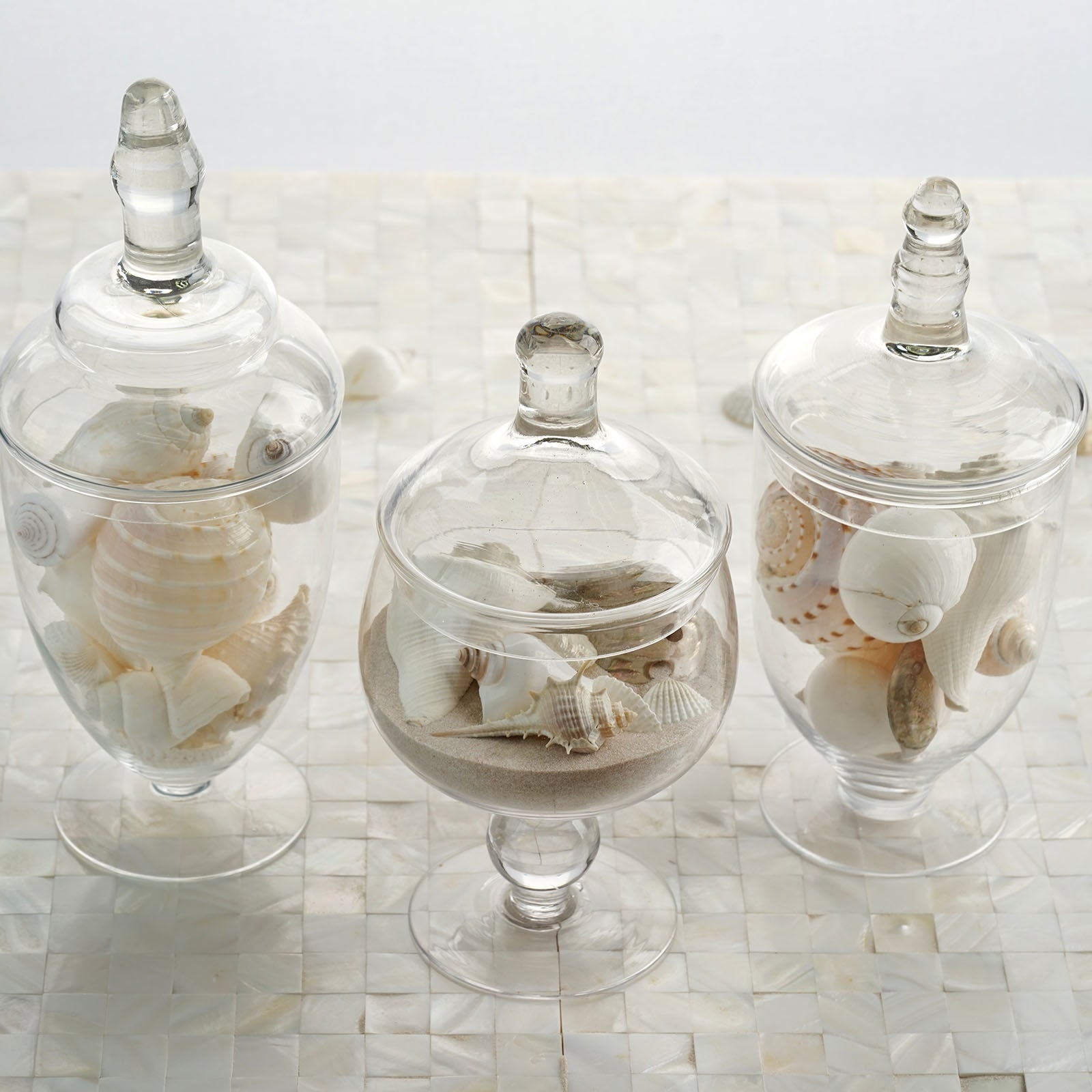 Clear glass apothecary jars with snap-on lids and decorative footed bases.