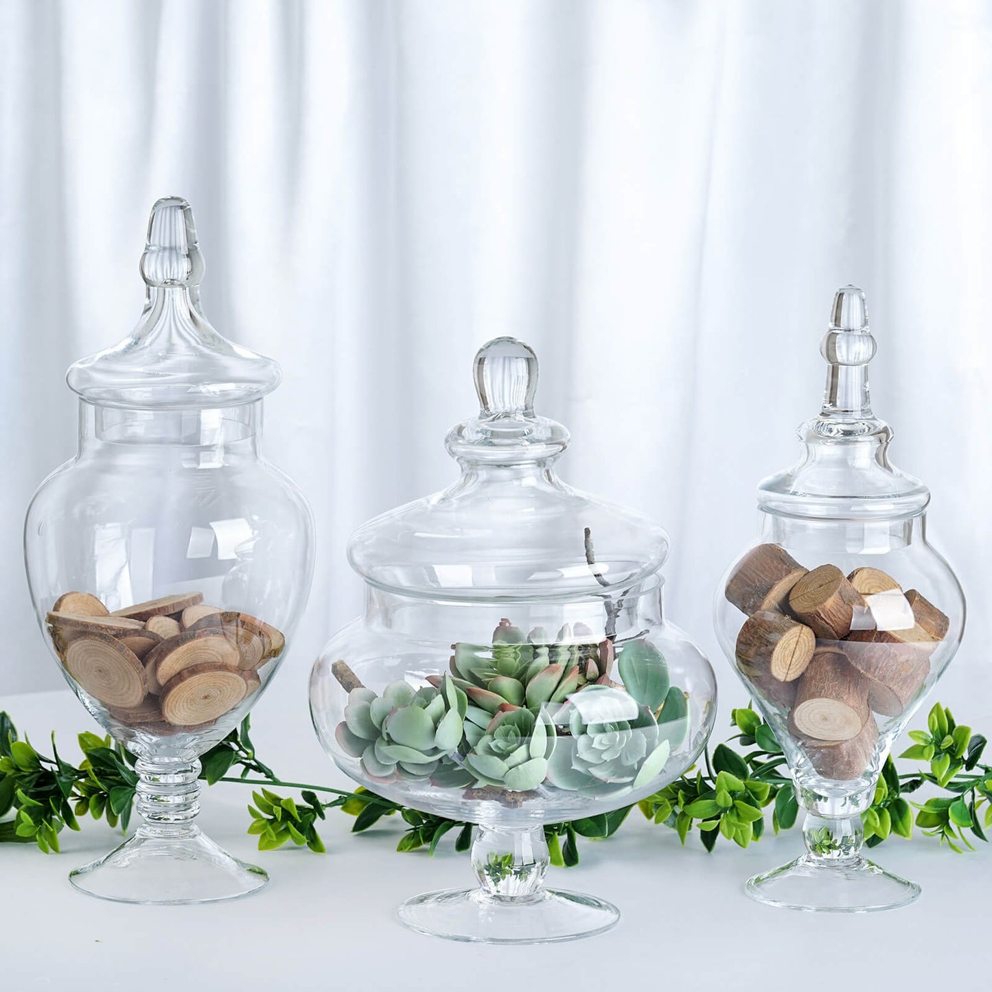 Clear glass pedestal apothecary jars set with snap-on lids.