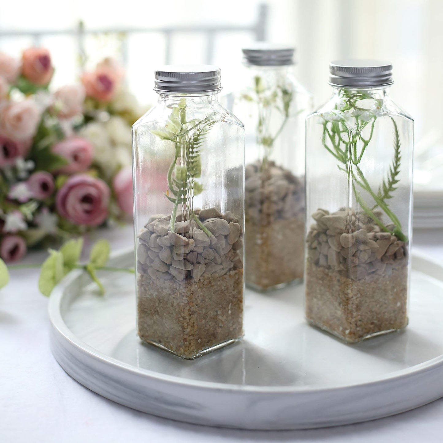 Clear glass jars with aluminum caps for storage, filled with decorative stones and greenery.