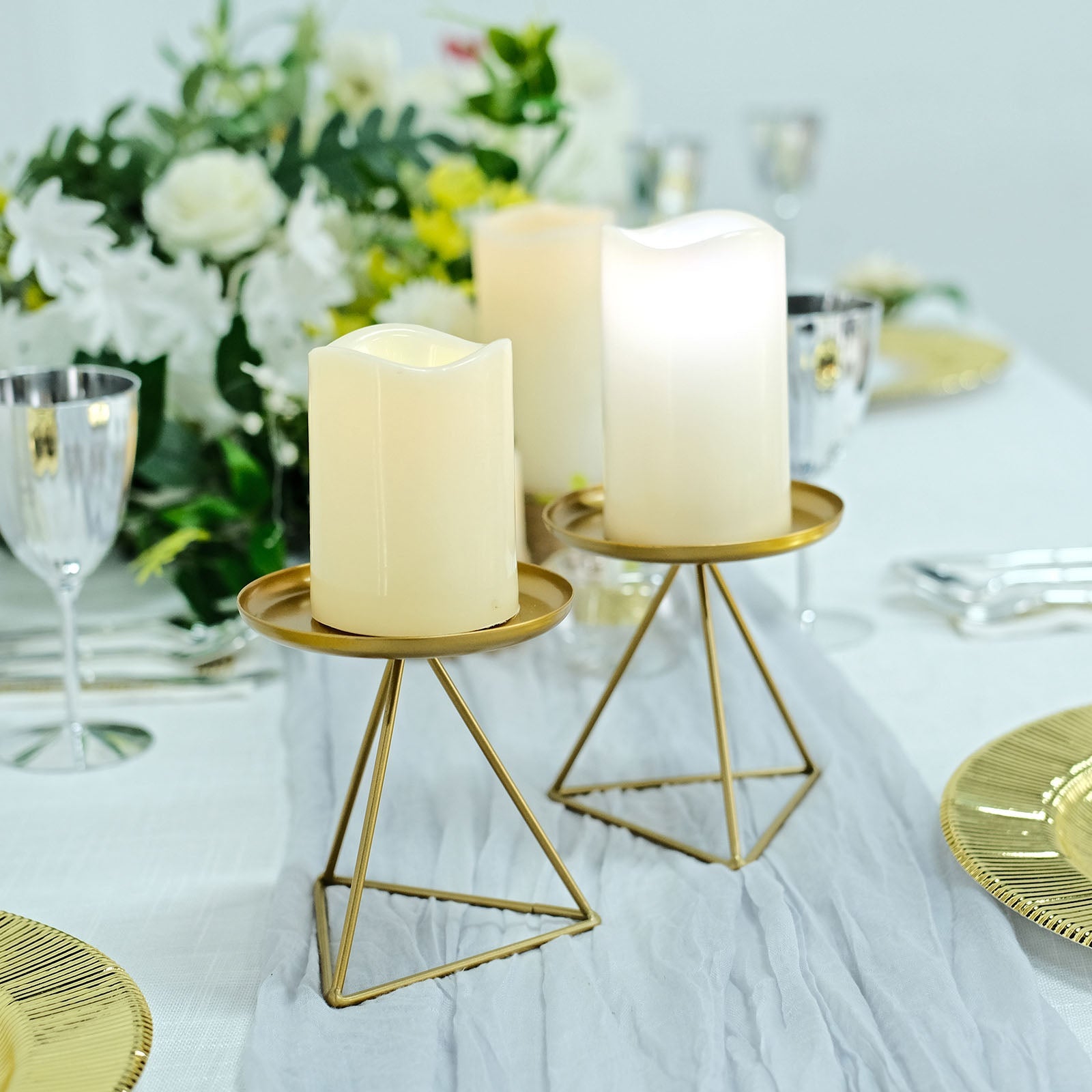 Gold metal triangle base candle holders with pillar candles on a table.