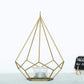 Gold geometric tealight candle holder with open frame design.