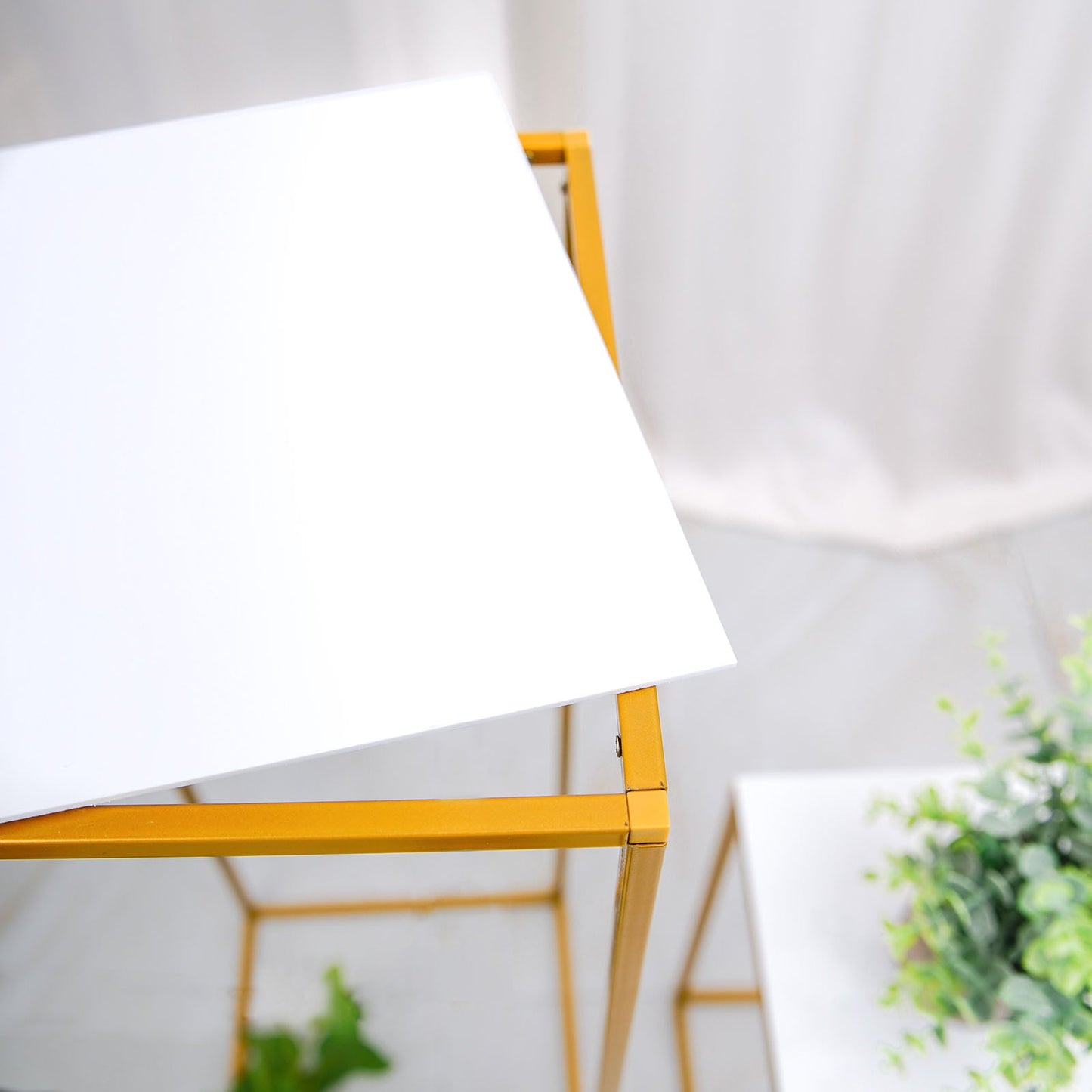 White acrylic square plexiglass sheets on a yellow table with greenery.