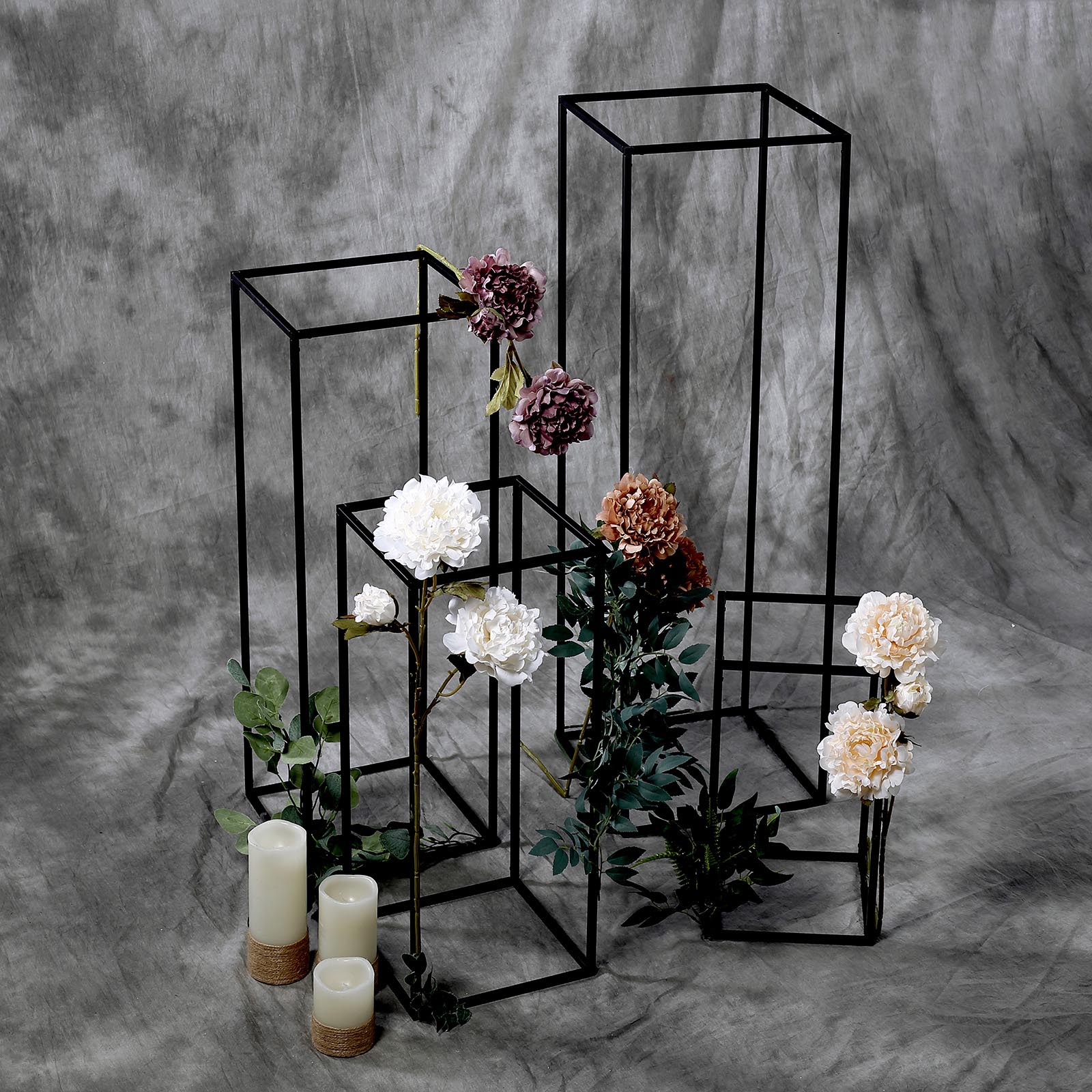 Matte black metal flower stands with floral arrangements and candles.