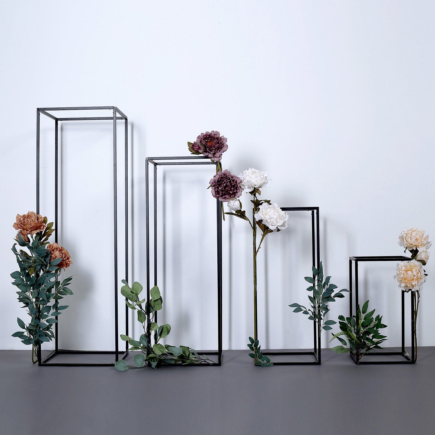 Matte black metal frame flower stands with artificial flowers and greenery.