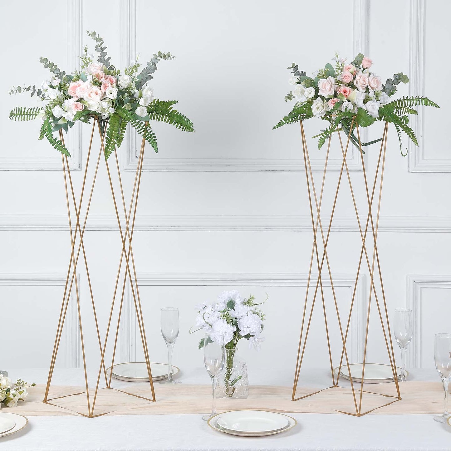 Gold geometric crisscross metal frame flower stands with elegant floral arrangements.