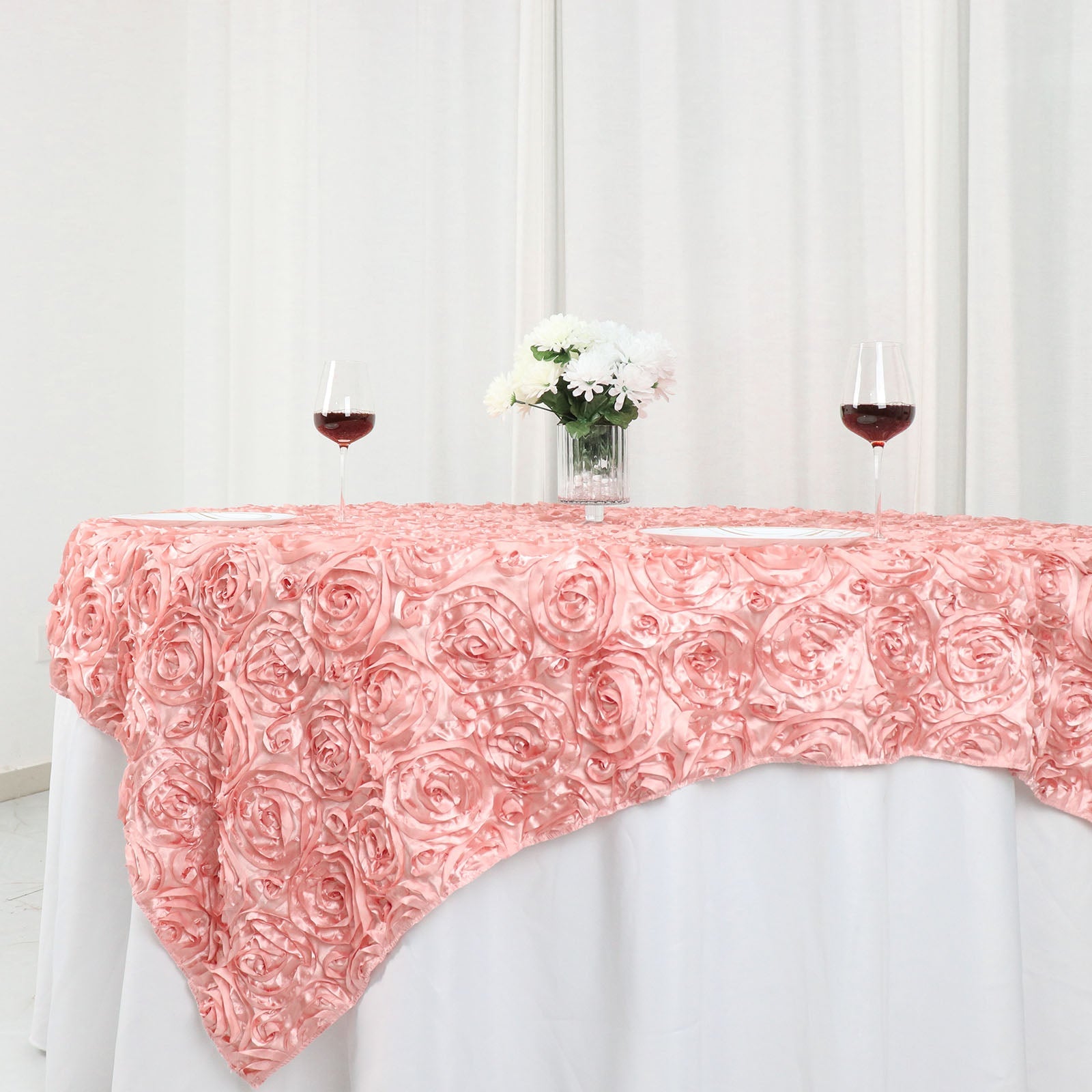 Dusty rose 3D rosette satin table overlay on a square table.