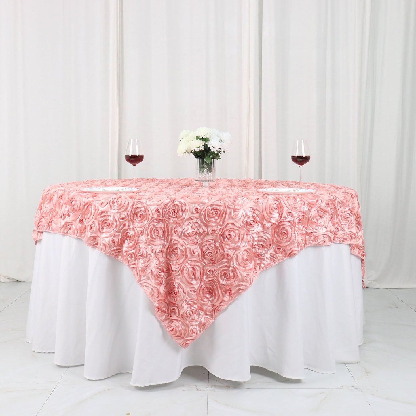 Dusty rose 3D rosette satin table overlay on a round table with white tablecloth.