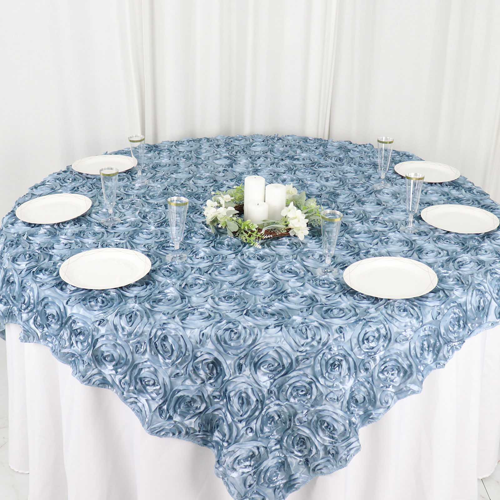 Dusty blue 3D rosette satin table overlay on a round table with decorative items.