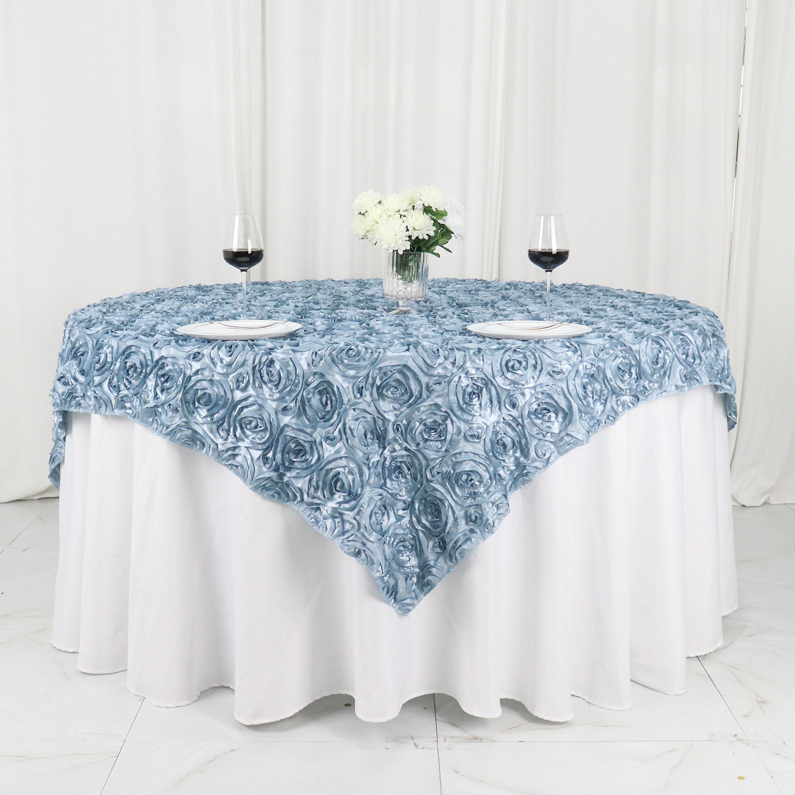Dusty blue 3D rosette satin table overlay on a round table with white linens.