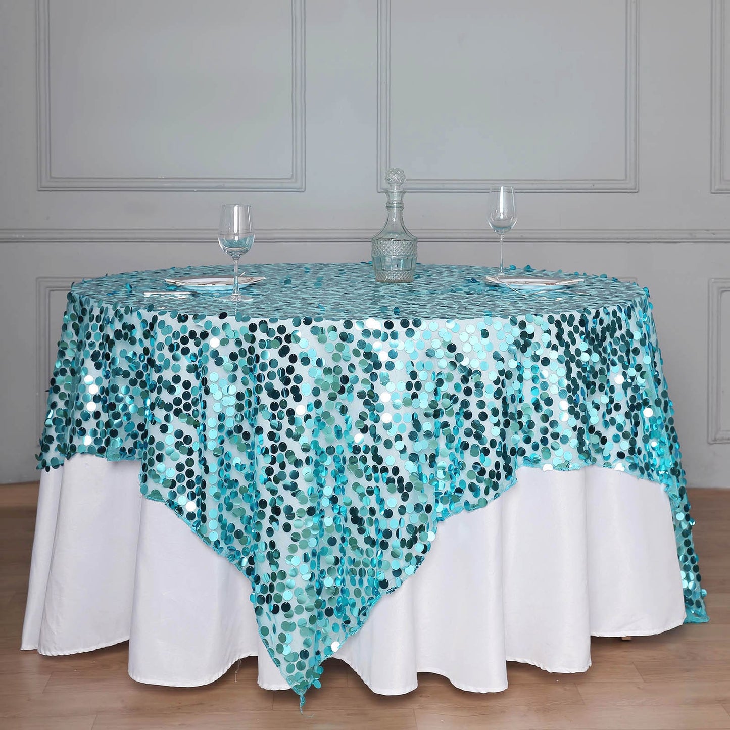 Turquoise sequin table overlay on a round table with a white tablecloth.