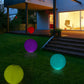 Colorful inflatable glow balls in a garden, featuring purple and teal lights.