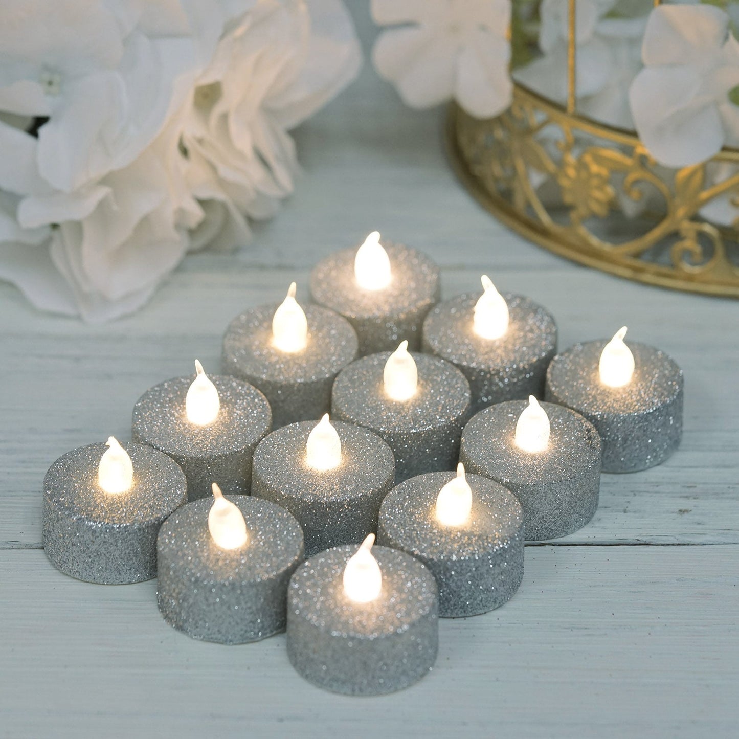 Silver glittered LED tealight candles arranged on a light surface.