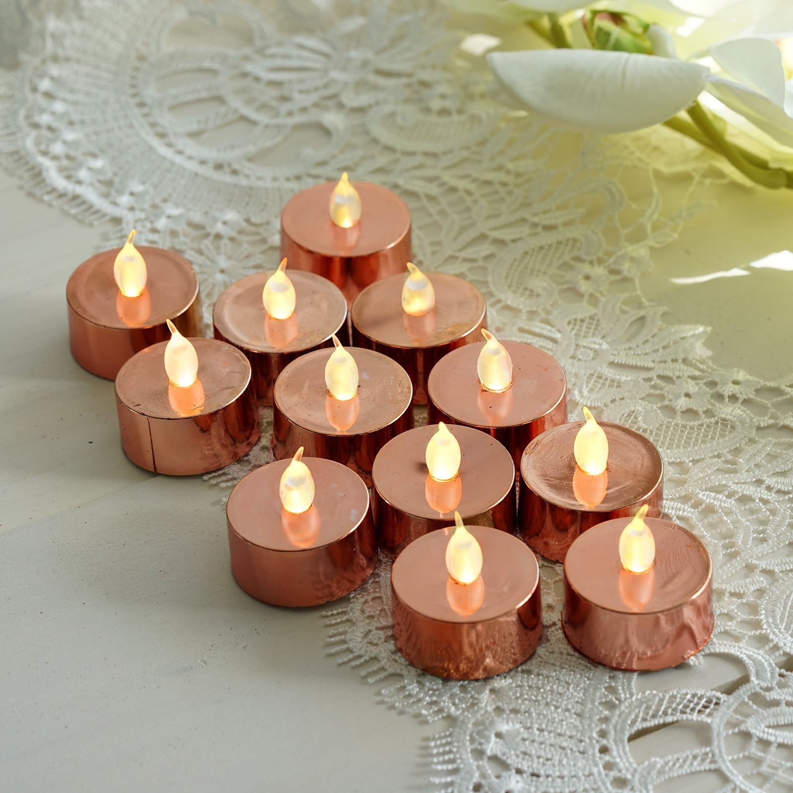 Rose gold LED tealight candles arranged on a lace surface.