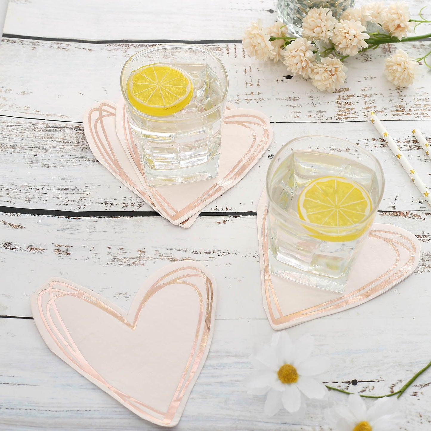 Rose gold heart-shaped cocktail napkins on a rustic table with drinks.