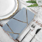 Dusty blue geometric gold cloth dinner napkin on a rustic table setting.