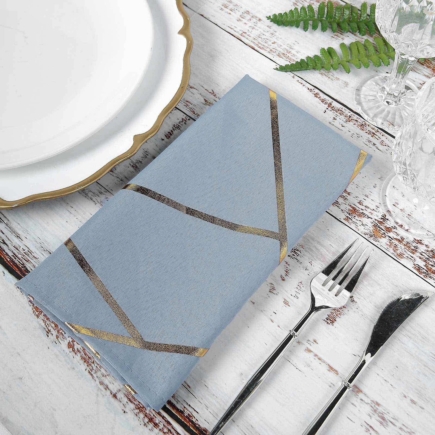 Dusty blue geometric gold cloth dinner napkin on a rustic table setting.