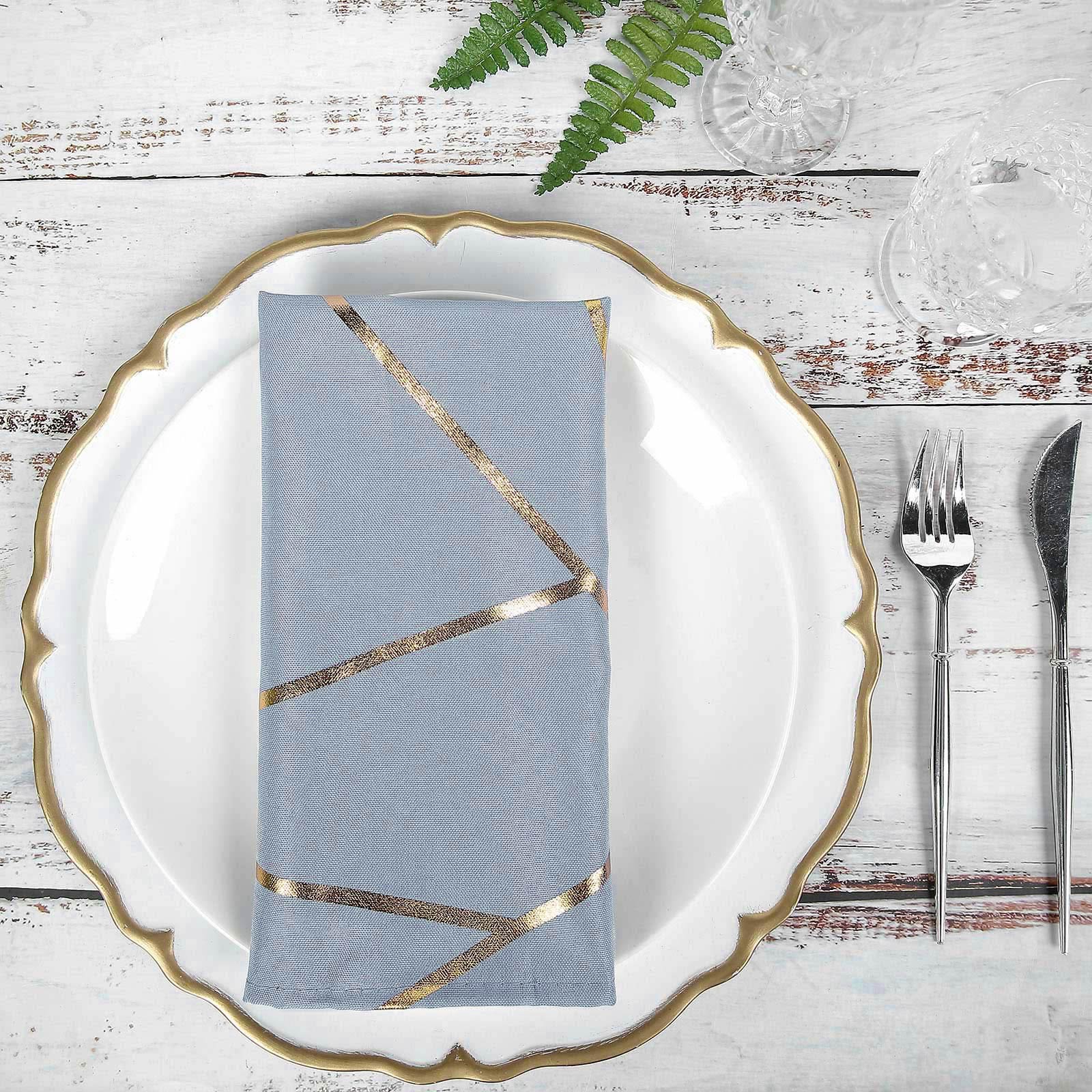 Modern dusty blue and geometric gold cloth dinner napkin on a decorative plate.