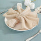 Beige slubby textured cloth dinner napkin on a plate with silverware.