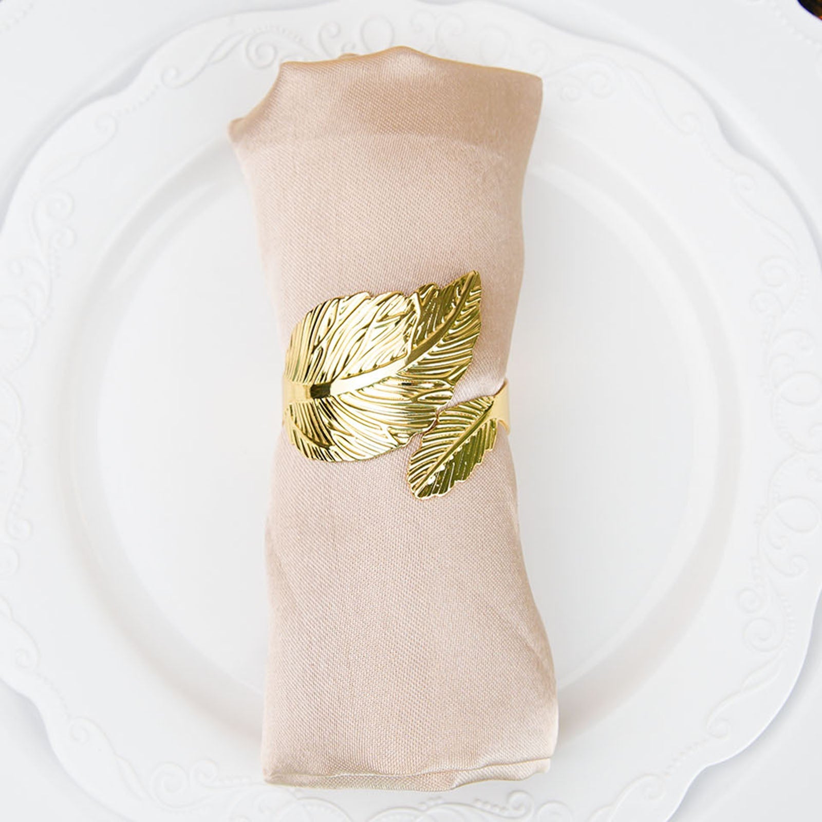 Metallic gold ornate leaf napkin ring on a linen napkin.
