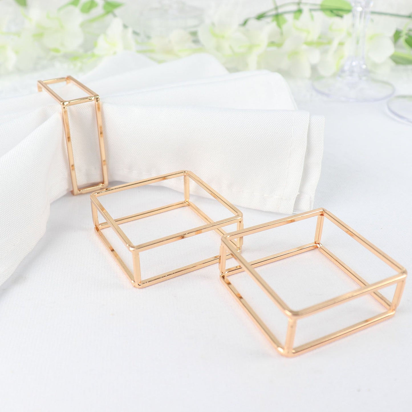 Gold metal hollow square napkin rings on white napkins.