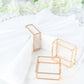 Gold metal hollow square napkin rings on a white table setting.