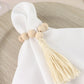 Cream wood bead napkin ring with tassel on white napkin.