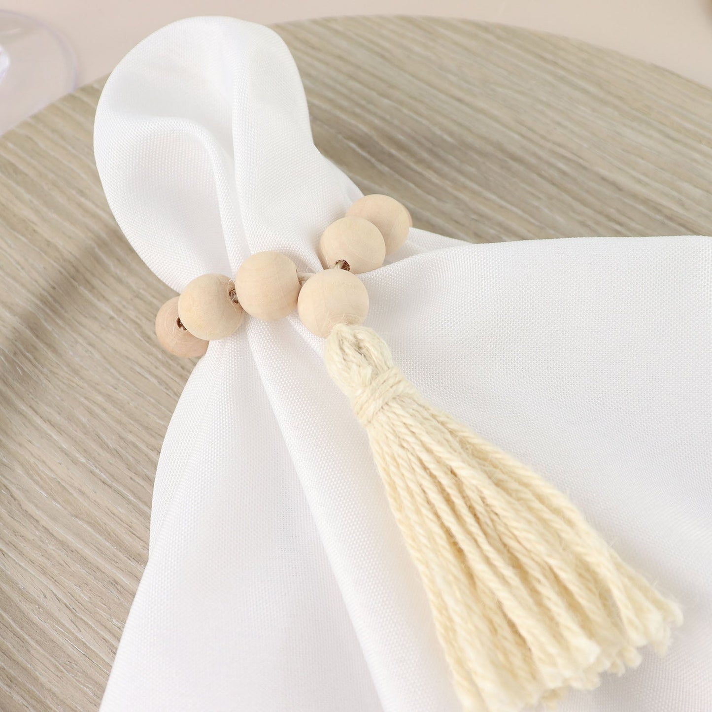 Cream wood bead napkin ring with tassel on white napkin.