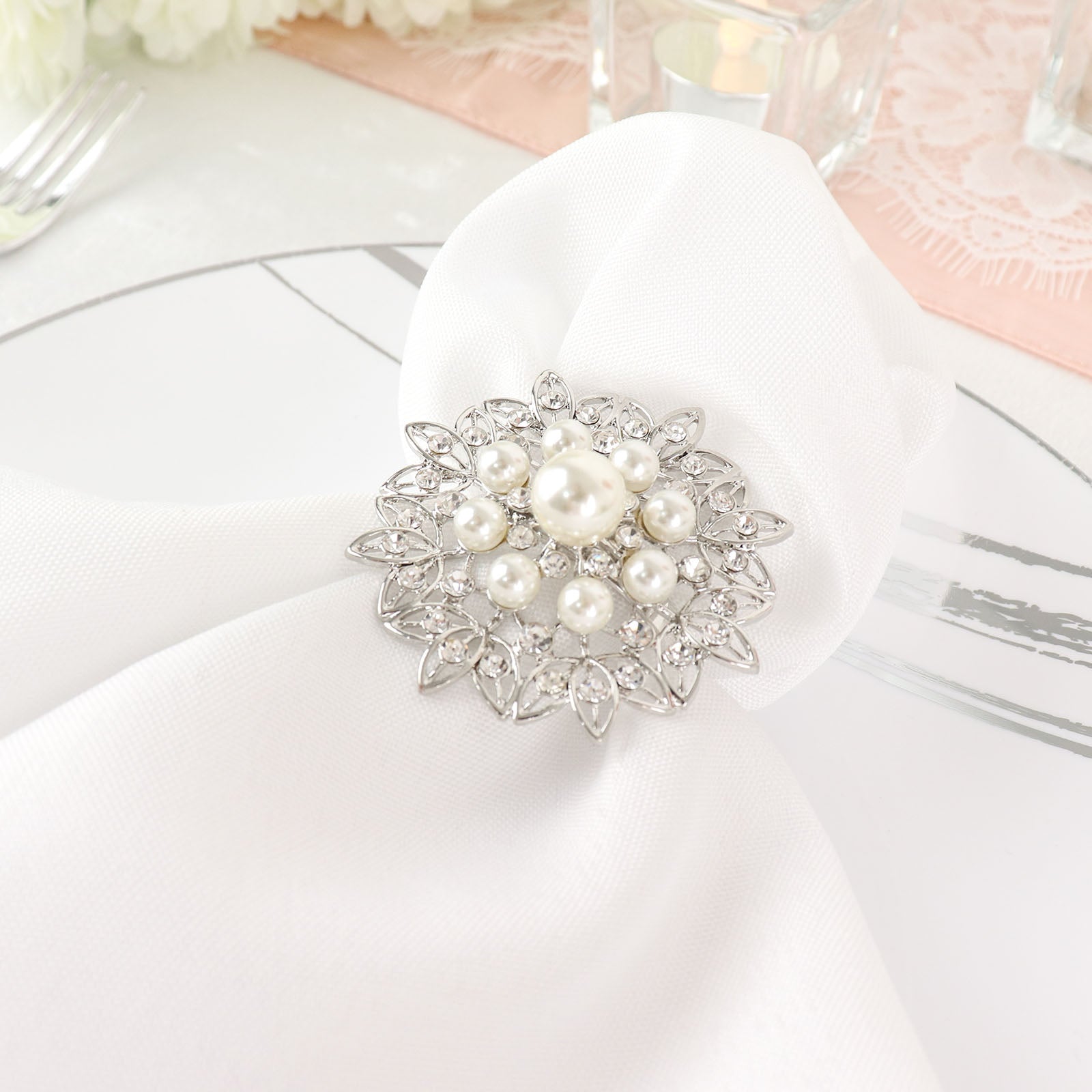 Silver metal napkin ring with pearl and diamond rhinestones on a white napkin.