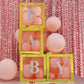 Iridescent alphabet stickers on yellow blocks with pink balloons.