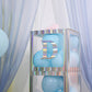 Iridescent alphabet sticker "D" on a display with blue balloons.