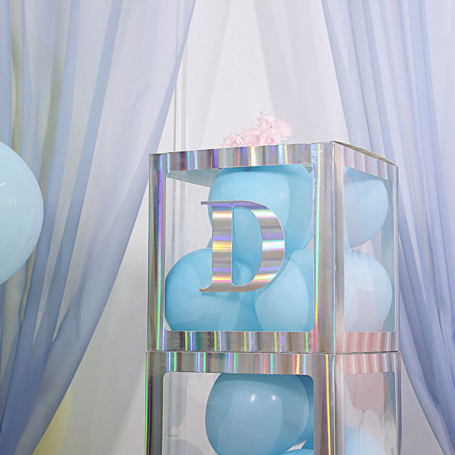 Iridescent alphabet sticker "D" on a display with blue balloons.