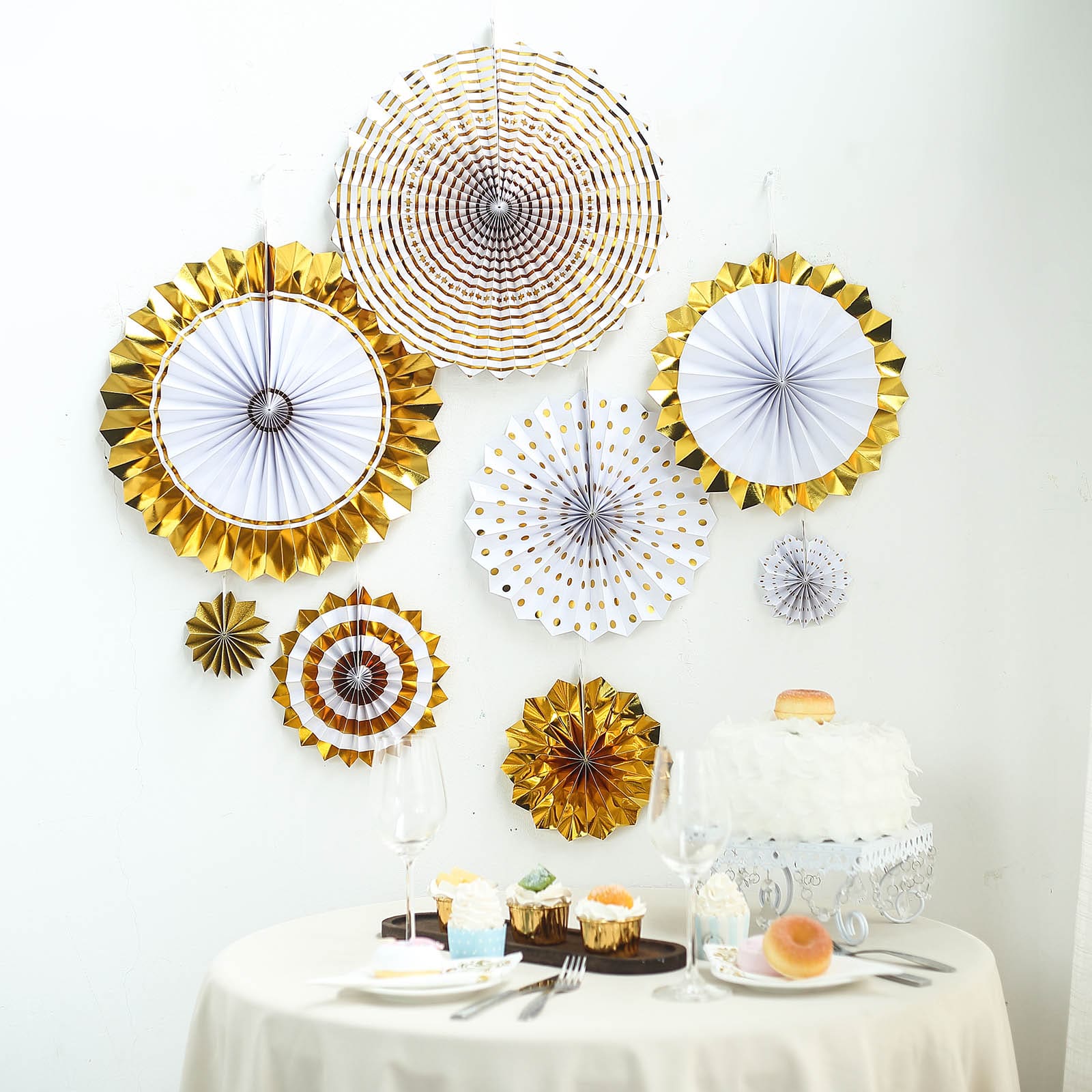 Gold and white hanging paper fan decorations in various sizes on a wall backdrop.