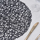 Black decorative woven round placemat on a table setting.