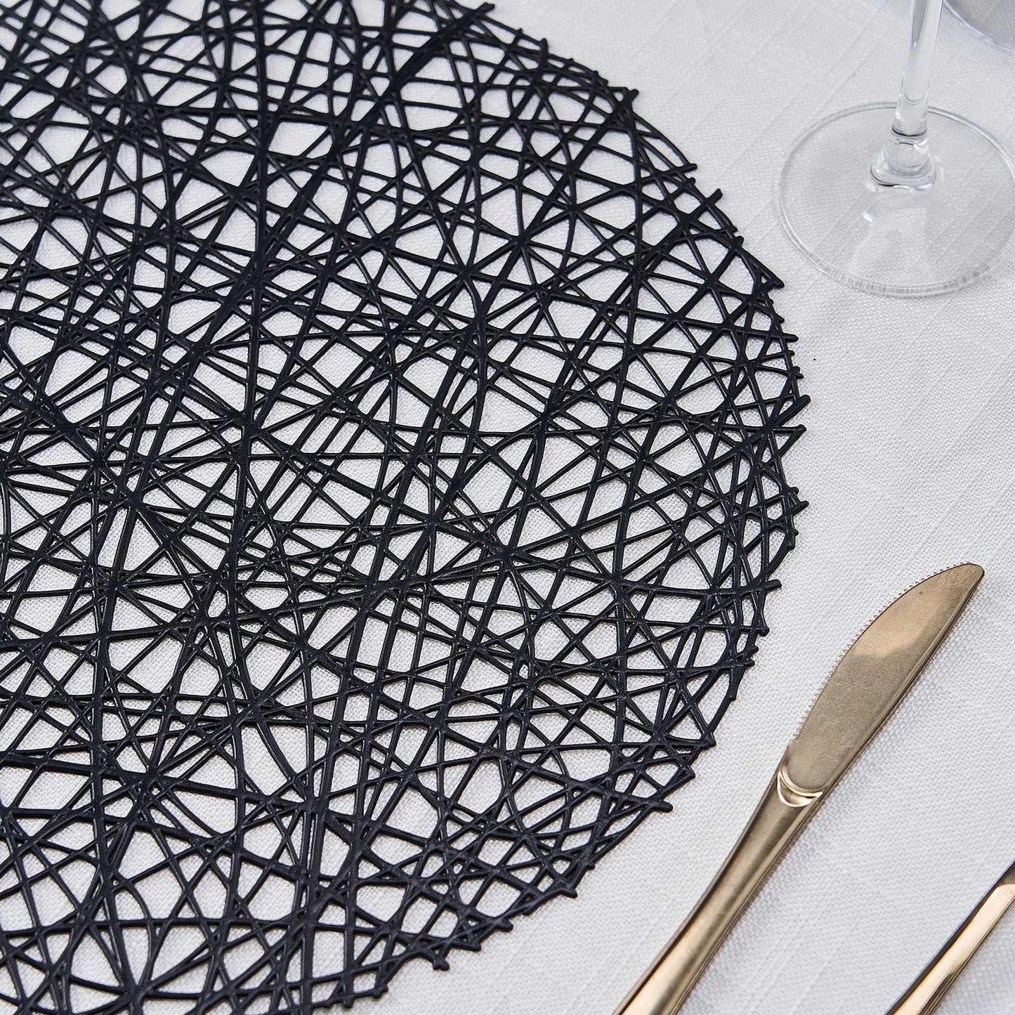 Black decorative woven round placemat on a table setting.