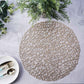 Champagne metallic woven round placemat on a textured surface.